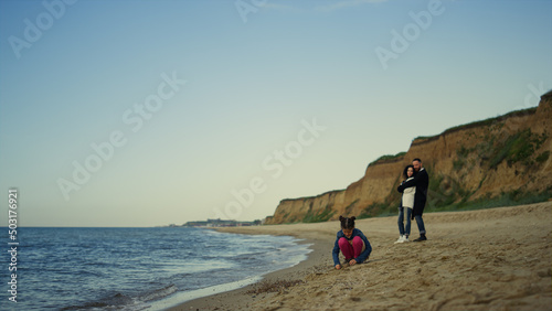 Young family enjoy vacation at ocean beach nature. Kid play by parents outdoors