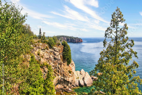 A view of Lake Superior on a sunny summer day as seen from a rocky tree-lined cliff.