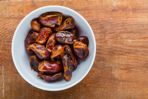Dates in a bowl on a wooden table save a place.