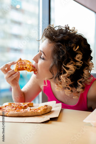 a young woman is wearing pink T-shirt eating pizza in a cafe