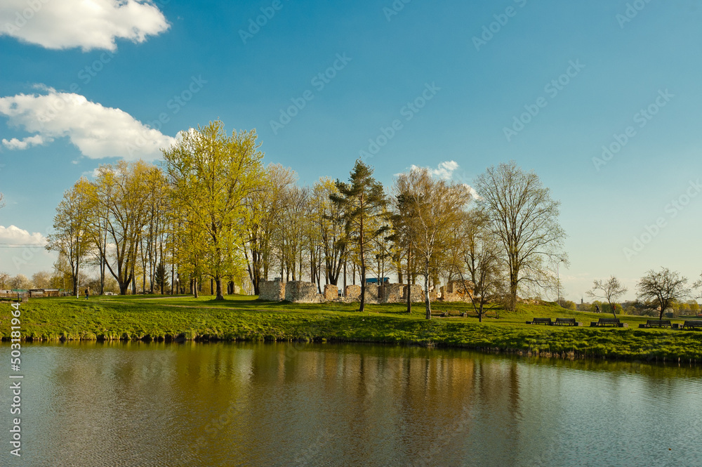 a pond in the park, in the photo a small pond in the recreation park, trees in the background, the ruins of an old building and a blue sky with clouds
