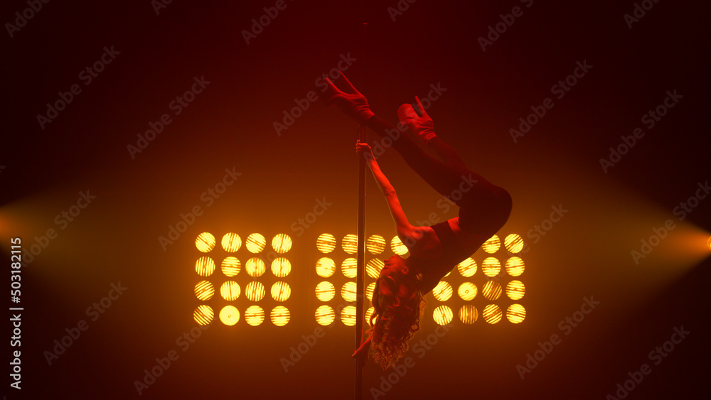 © stockbusters - Woman performing poledance tricks in spotlights. Blonde making twine on pylon. © stockbusters - Woman performing poledance tricks in spotlights. Blonde making twine on pylon.