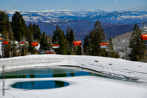 Orange bubble chair lift at Park City Canyons Ski Area in Utah. Late spring weather conditions. View to the valley with range of the mountains and pond.