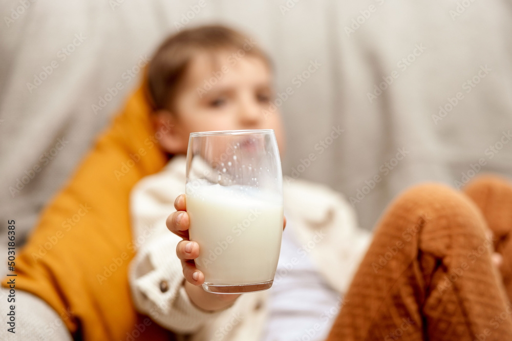 Little adorable boy sitting on the couch at home and drinking milk. Fresh milk in glass, dairy healthy drink. Healthcare, source of calcium, lactose. Preschool child with casual clothing. Little adorable boy sitting on the couch at home and drinking milk. Fresh milk in glass, dairy healthy drink. Healthcare, source of calcium, lactose. Preschool child with casual clothing.