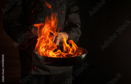 Obraz na plátne The chef cooking food in pan with fire flame on black background