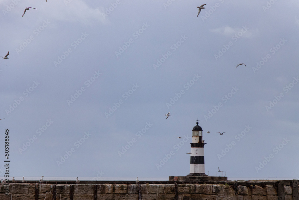 Iconic striped Seaham lighthouse on pier with clouds and sea walls