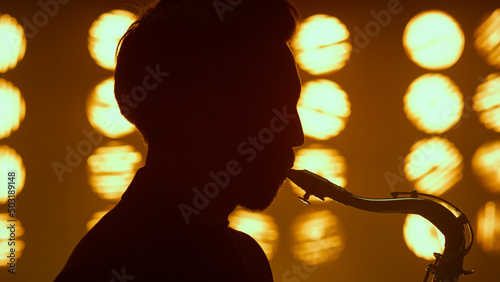 Silhouette guy blowing saxophone on stage closeup. Young saxophonist performing.
