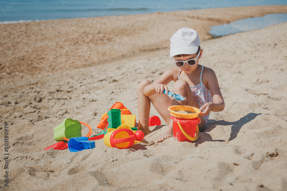 one little toddler girl 4 years old sits on the beach and play with the toys one little toddler girl 4 years old sits on the beach and play with the toys