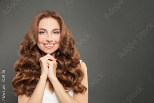 Portrait of pretty woman with long curly beautiful brown hair and cute friendly smile on dark gray background.