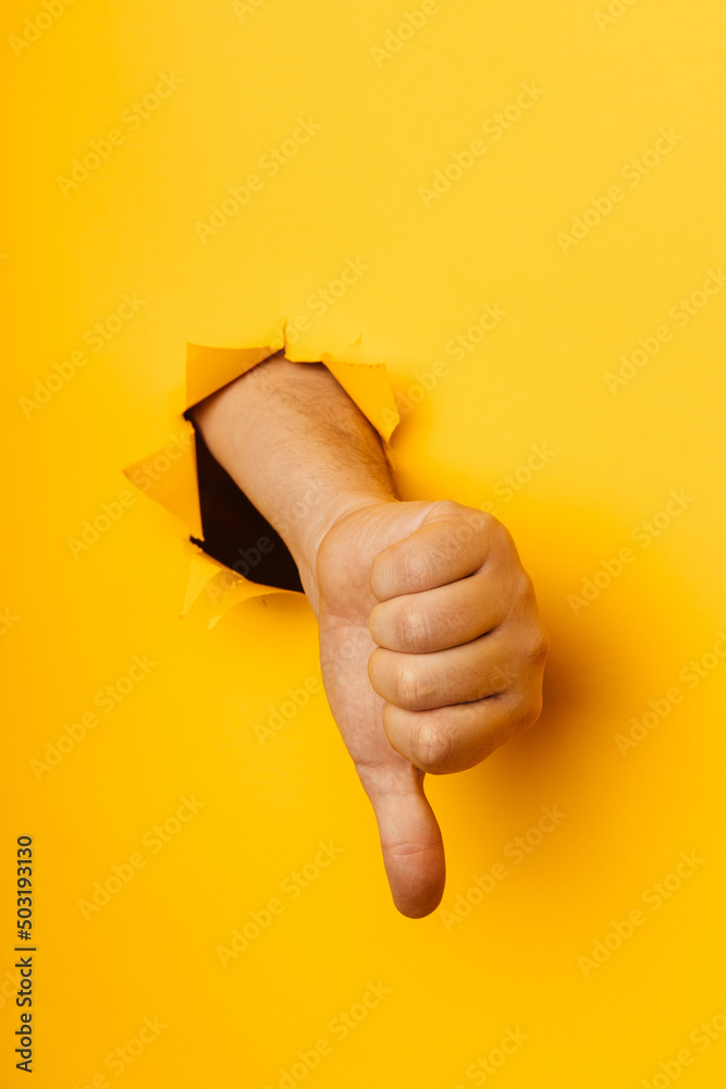 Hand showing a thumb down through ripped hole in yellow paper ...