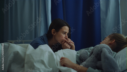 Mother sitting sick daughter after surgical treatment in modern hospital ward. 