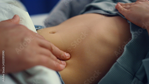 Doctor hands checking stomach of little sick girl in hospital ward closeup. 