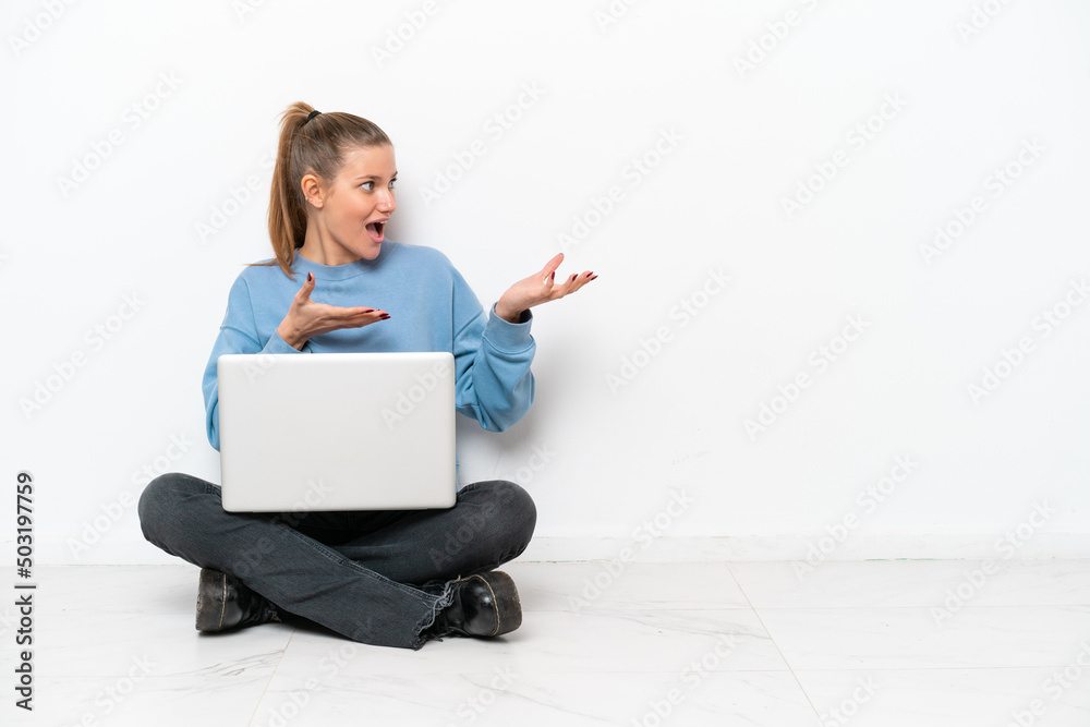Young woman with a laptop sitting on the floor with surprise facial expression Young woman with a laptop sitting on the floor with surprise facial expression