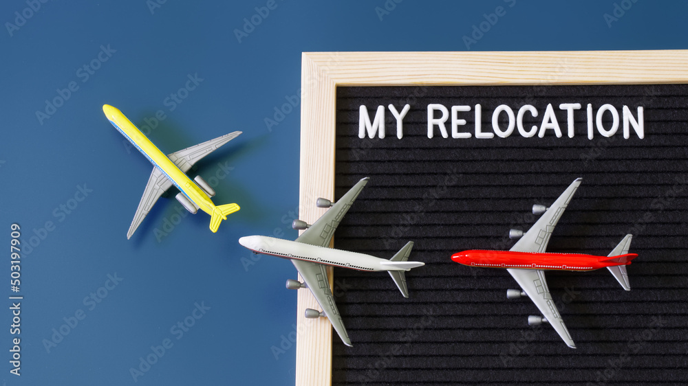 Toy passenger planes next to a felt board with the inscription my relocation. The concept of moving, migration and relocation. Blue background. Toy passenger planes next to a felt board with the inscription my relocation. The concept of moving, migration and relocation. Blue background.