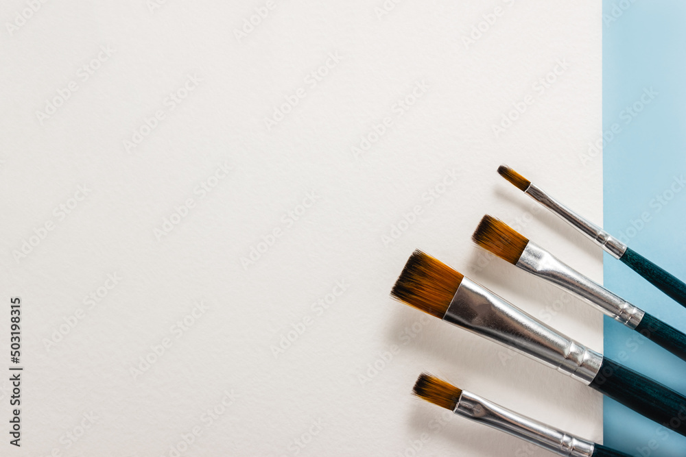 Paint brushes on white canvas and blue background. Selective focus, copy space Paint brushes on white canvas and blue background. Selective focus, copy space