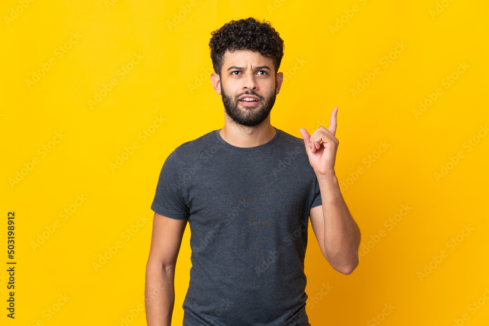Fototapeta premium Young Moroccan man isolated on yellow background thinking an idea pointing the finger up