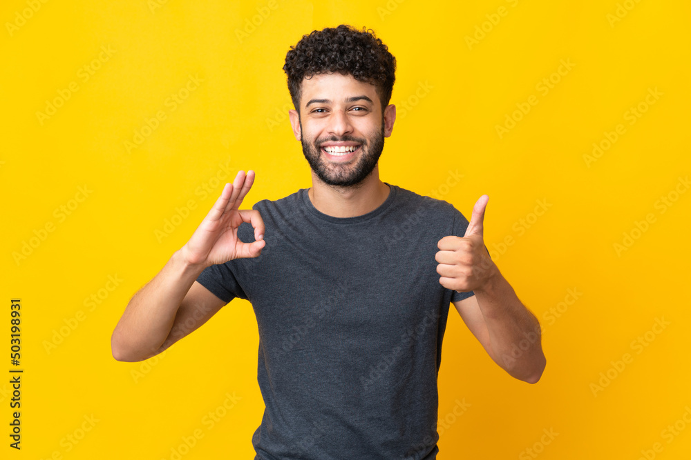 Young Moroccan man isolated on yellow background showing ok sign and thumb up gesture Young Moroccan man isolated on yellow background showing ok sign and thumb up gesture