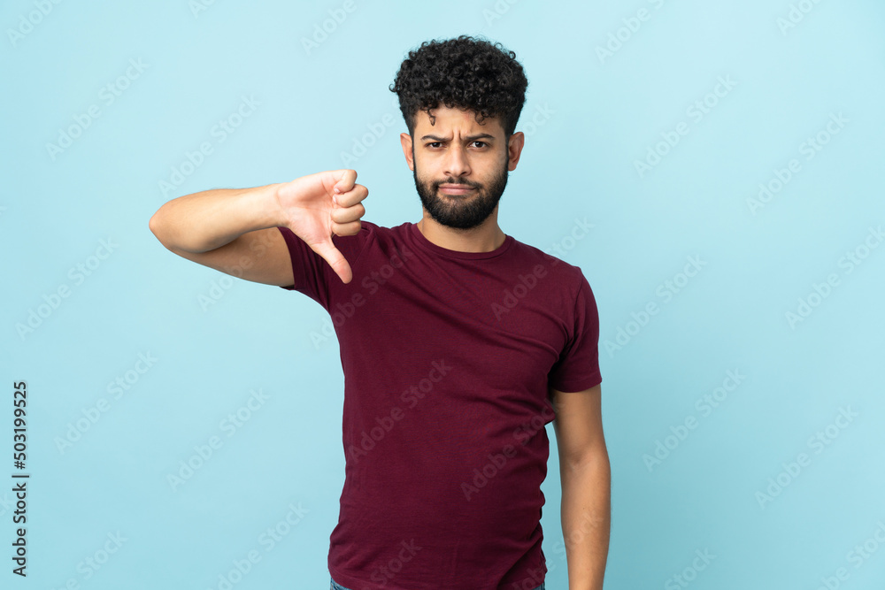 Young Moroccan man isolated on blue background showing thumb down with negative expression Young Moroccan man isolated on blue background showing thumb down with negative expression