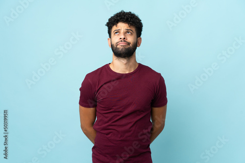 Young Moroccan man isolated on blue background and looking up