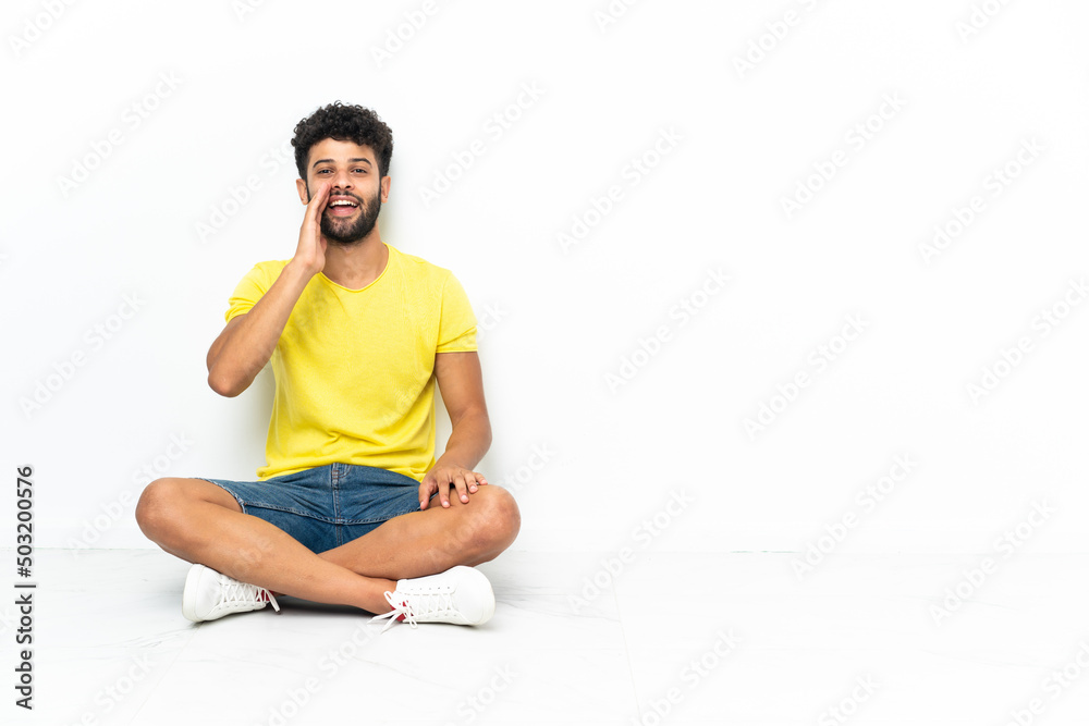 Fototapeta premium Young Moroccan handsome man sitting on the floor over isolated background shouting with mouth wide open