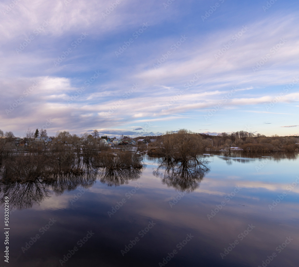 Fototapeta premium Cold spring evening. High water, the river overflowed its banks. Trees and bushes in the water.