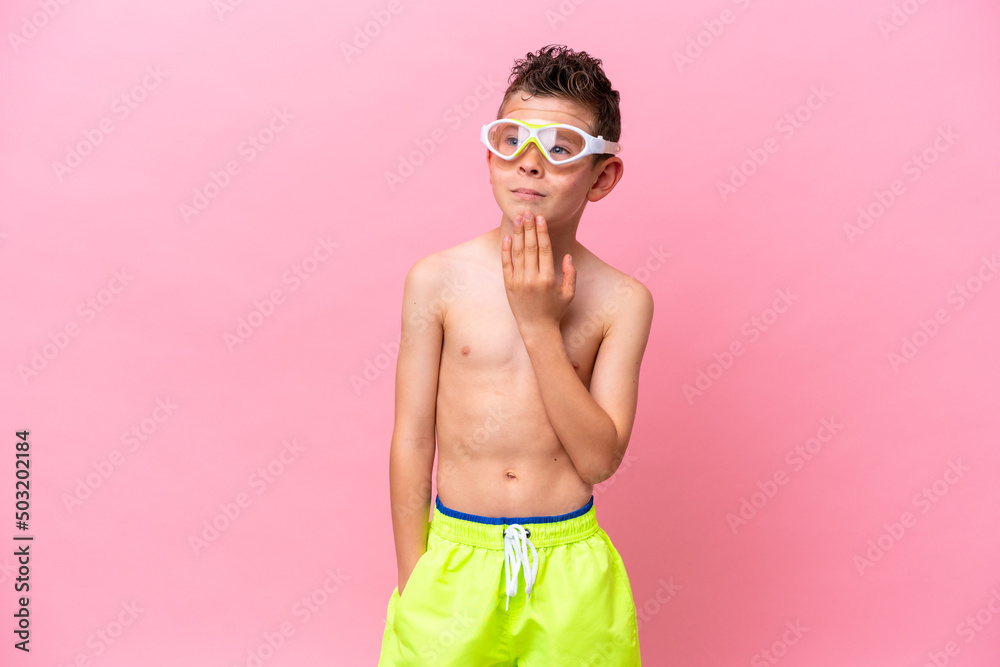 Little caucasian boy wearing a diving goggles isolated on pink background looking up while smiling Little caucasian boy wearing a diving goggles isolated on pink background looking up while smiling
