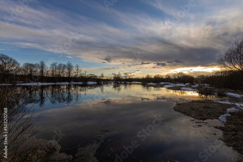 Epic spring landscape by the river. The flood of the river in early spring. A colorful sunset is reflected in the water. March evening landscape.