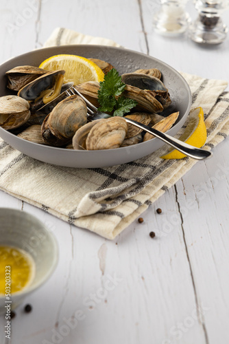 Steamed clams in a grey bowl on light background..