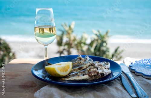 Sardines espeto prepared on skewers and open flame on fireplace with olive trees wood, served outdoor with glass of fino sherry and view on blue sea, Malaga, Andalusia, Spain