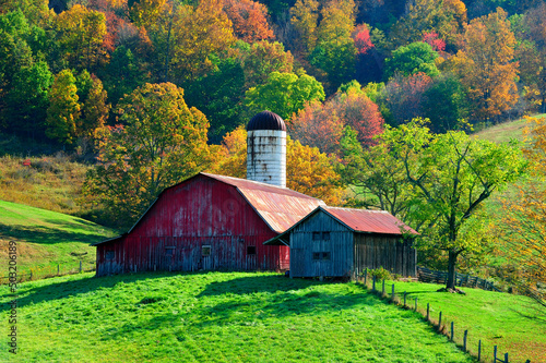 Large red barn on a hillside surrounded by beautiful autumn colors