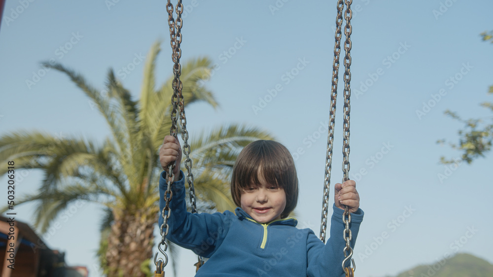 On sunny spring day, little boy or baby is smiling and having fun, swinging on the cute cheerful swing, enjoying playing in the park with his smiling cute or cute facial expressions