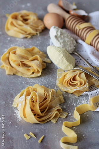 Fresh homemade pasta on a wooden table with rolling pin and toasted flour, noodles, rustic composition.
