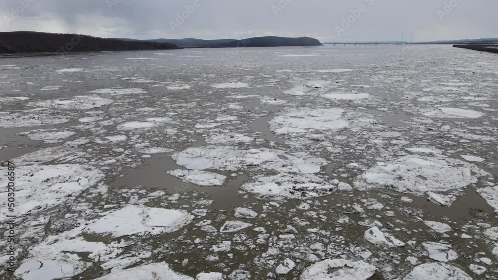 Ice Drift Occurs on the River next to the Island with Forest and Mountain Ridge, Aerial view above, Reflection in Water Ice Drift Occurs on the River next to the Island with Forest and Mountain Ridge, Aerial view above, Reflection in Water