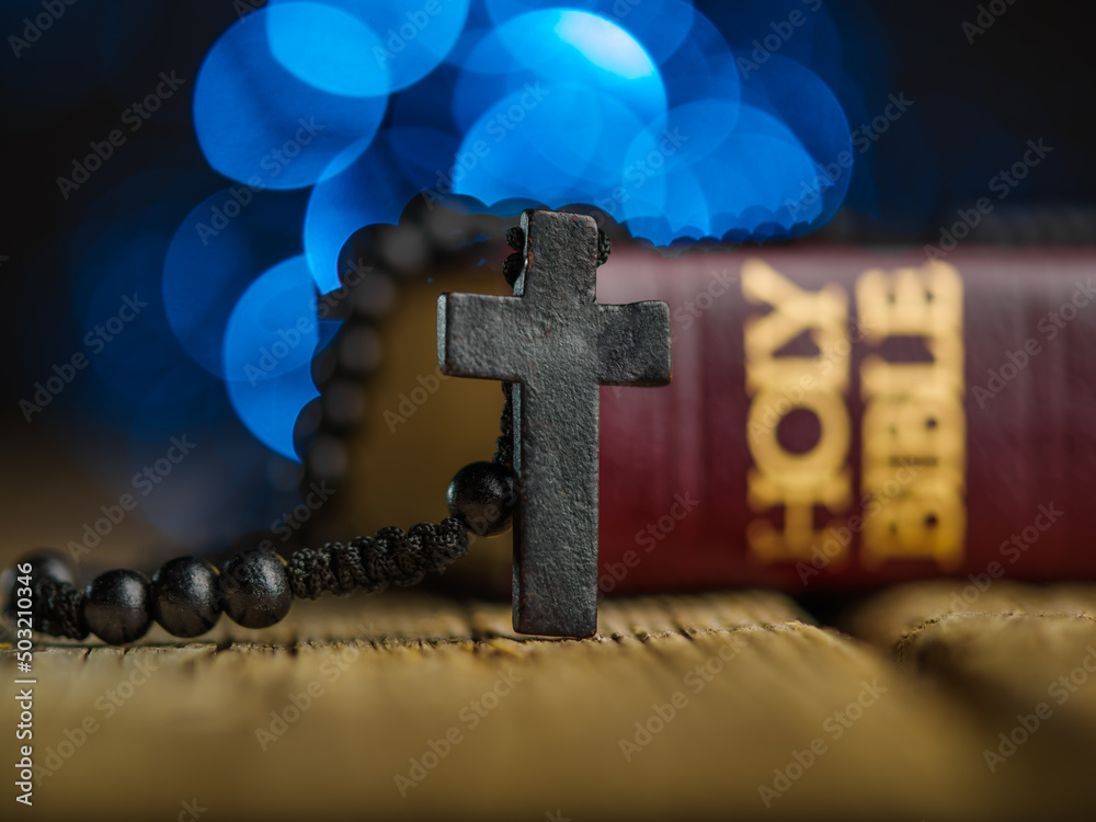 Φωτογραφία On a simple wooden table is a Catholic cross and a Holy Bible against a blue background with twinkling lights