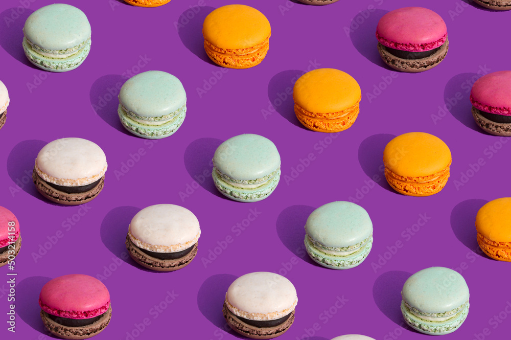 Fototapeta premium Colorful macarons ona dark purple background. Summer pattern of sweet food. Aesthetic still life concept. Trendy colors with strong contrast.