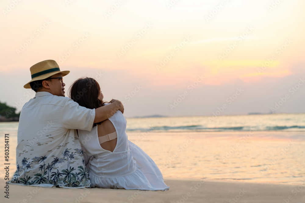 Happy family Asian couple sitting on tropical beach and embracing each other at summer sunset. Husband and wife relax and enjoy outdoor lifestyle romantic holiday travel beach vacation at the sea Happy family Asian couple sitting on tropical beach and embracing each other at summer sunset. Husband and wife relax and enjoy outdoor lifestyle romantic holiday travel beach vacation at the sea