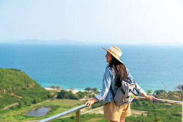 Young beautiful Asian woman with backpack solo travel on tropical island mountain peak in summer sunny day. Cheerful female relax and enjoy outdoor lifestyle in summer beach holiday vacation trip