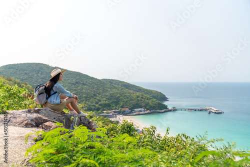 Young beautiful Asian woman with backpack solo travel on tropical island mountain peak in summer sunny day. Cheerful female relax and enjoy outdoor lifestyle in summer beach holiday vacation trip