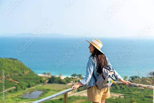 Young beautiful Asian woman with backpack solo travel on tropical island mountain peak in summer sunny day. Cheerful female relax and enjoy outdoor lifestyle in summer beach holiday vacation trip