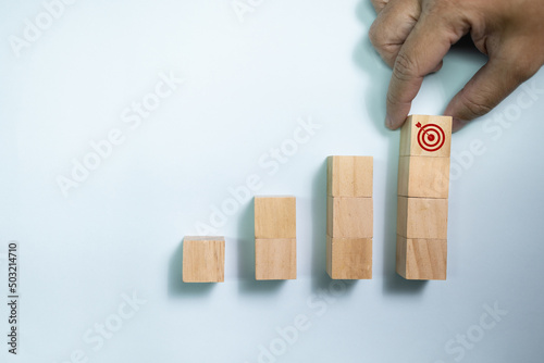 Top view hand place wooden blocks set to step with icon arrow to target. Concept for growth business and targeting.