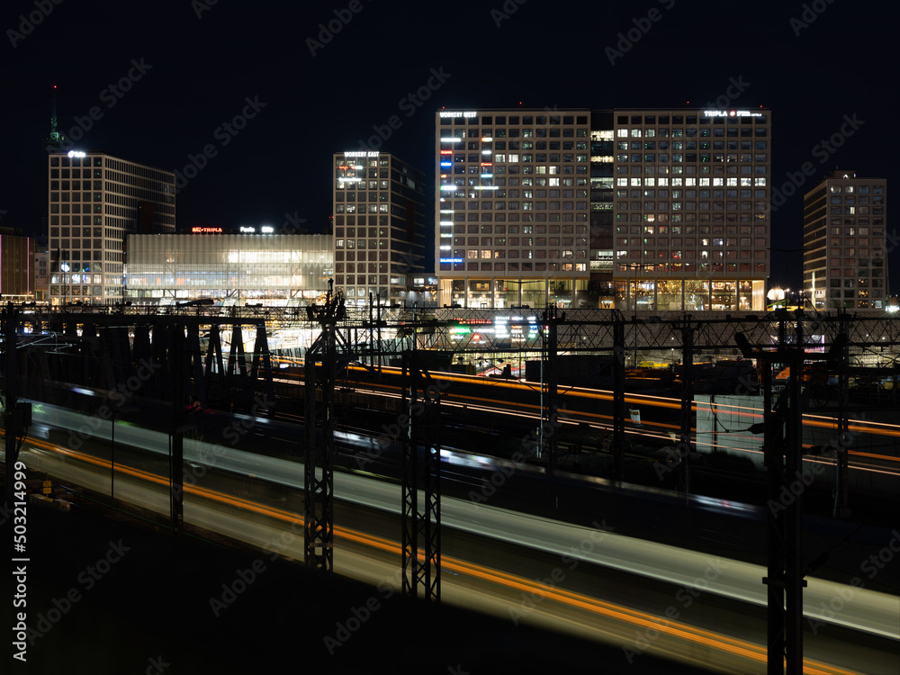 Fototapeta premium Modern financial district and a train station in the background. Passing by trains cast light trails in the foreground.