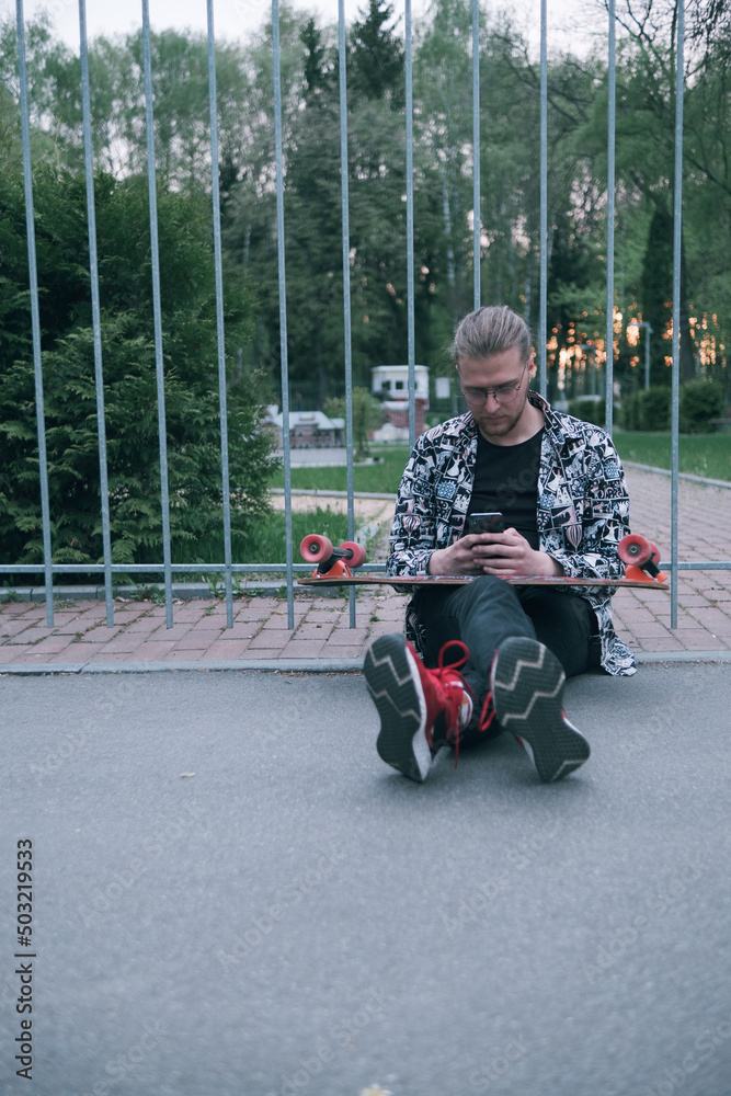 Young man using a cellphone while sitting at the skatepark. Young man using a cellphone while sitting at the skatepark.