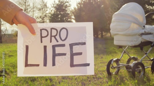 Hand of woman holding board with Pro Life words with baby trolley in background photo