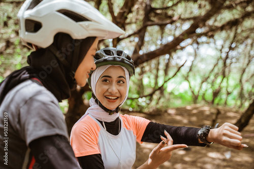 Two asian women cycling and one showing his watch during a cycling break in the park