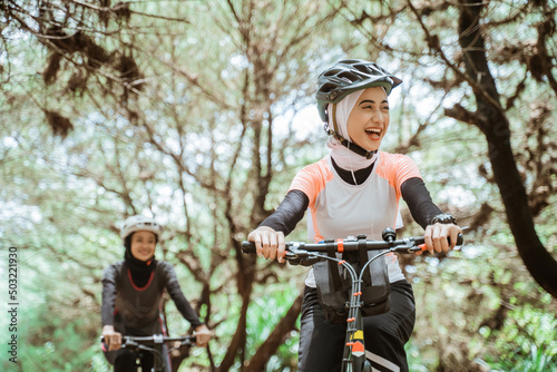 Happiness of beautiful young muslim woman wearing sportswear and helmet while cycling together outdoors