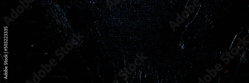 Dark creative background - rough linen canvas unevenly covered with black primer, reflections of light. Toning, blurring, selective focus.
