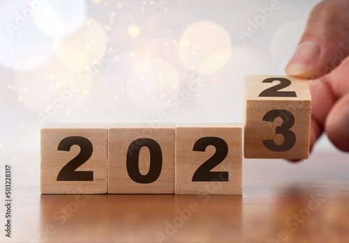 Anniversary, new year 2022 change to 2023. Man flip over wooden cube block. New year 2023 business goal concept