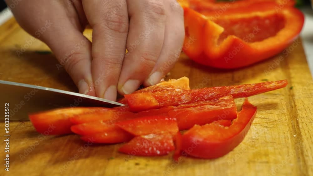 In the close-up, the cook is slicing red bell peppers on the cutting board. Vegetarian Cuisine. The concept of delicious and healthy food In the close-up, the cook is slicing red bell peppers on the cutting board. Vegetarian Cuisine. The concept of delicious and healthy food