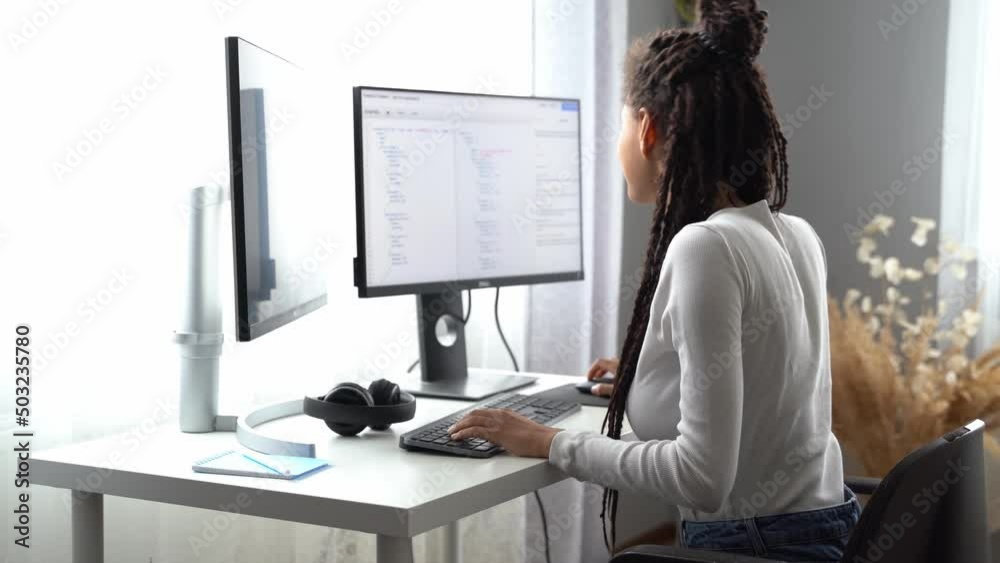 Back view of young professional woman programmer working from home sitting at desk