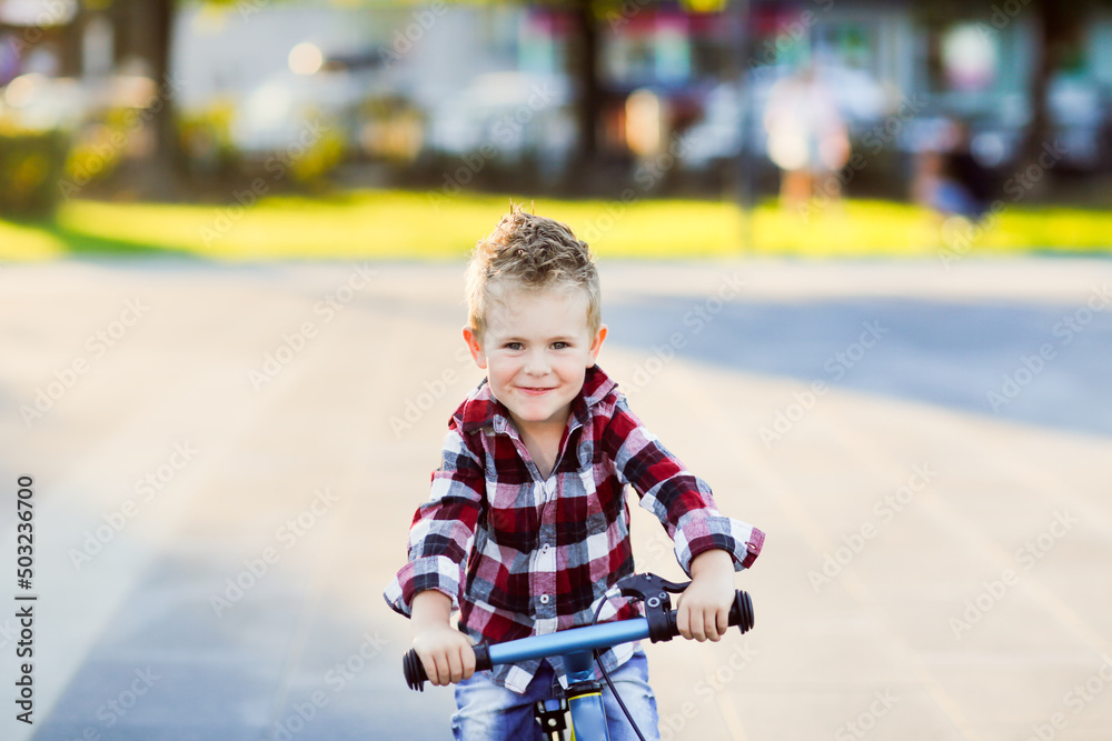 stylish European boy in shirt and jeans rides balance bike on asphalt. Child riding without helmet stylish European boy in shirt and jeans rides balance bike on asphalt. Child riding without helmet
